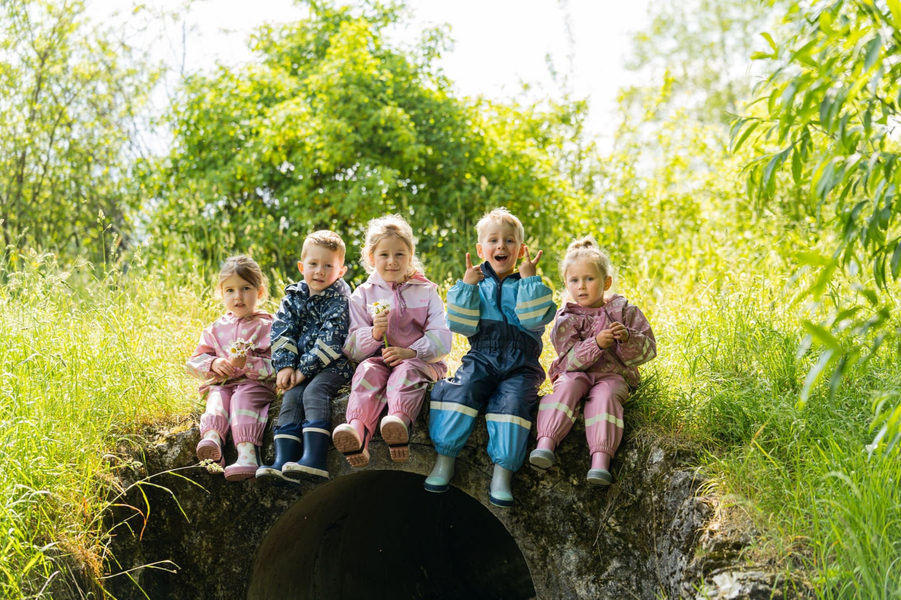 Kinder in Regenanzügen und Gummistiefeln im hohen Gras
